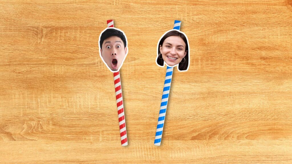 Two personalised face straws on a wooden background, one with a surprised face on a red and white straw, and the other with a smiling face on a blue and white straw.