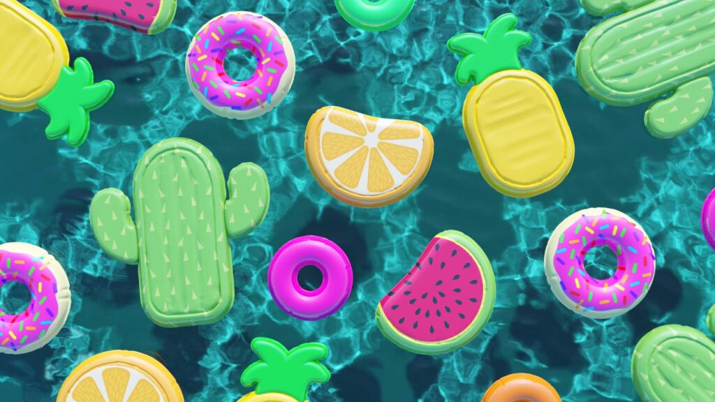 A variety of colourful pool floats shaped like fruits and donuts floating on water.