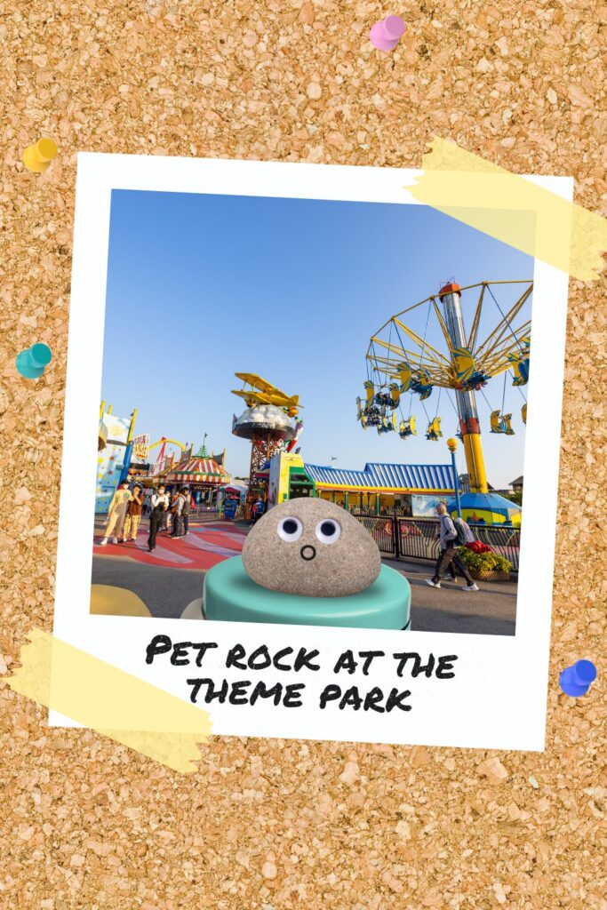 A pet rock with googly eyes sitting on a platform at a colourful theme park with rides and attractions in the background.