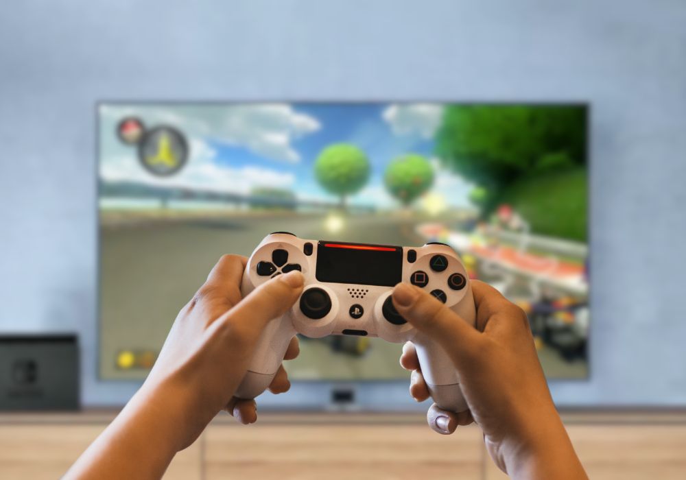 A person holding a game controller, playing a video game as part of a virtual birthday party.